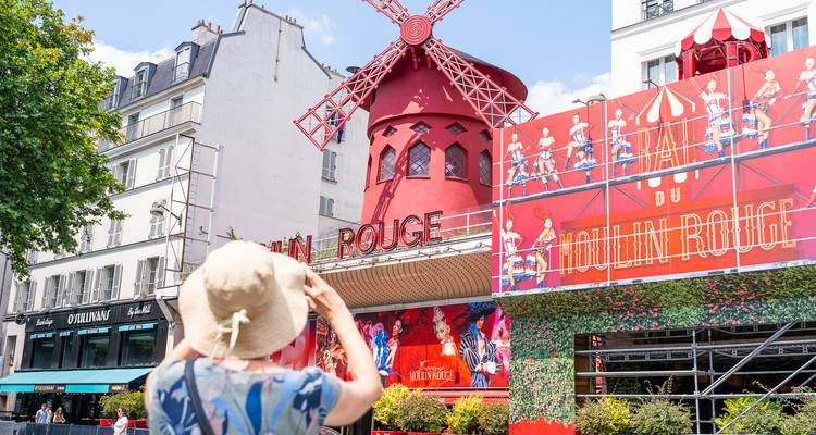Un visiteur photographie le moulin rouge vif du cabaret emblématique Moulin Rouge à Paris.