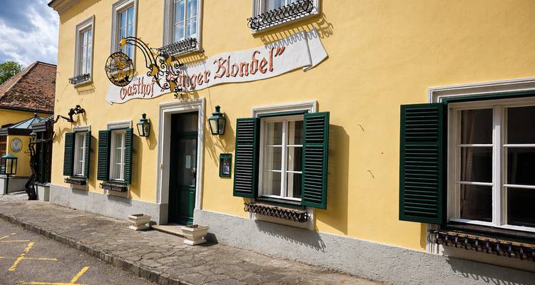 Vista soleada de una acogedora casa de huéspedes histórica de color amarillo con persianas verdes a lo largo de un callejón empedrado en un pequeño pueblo austriaco.