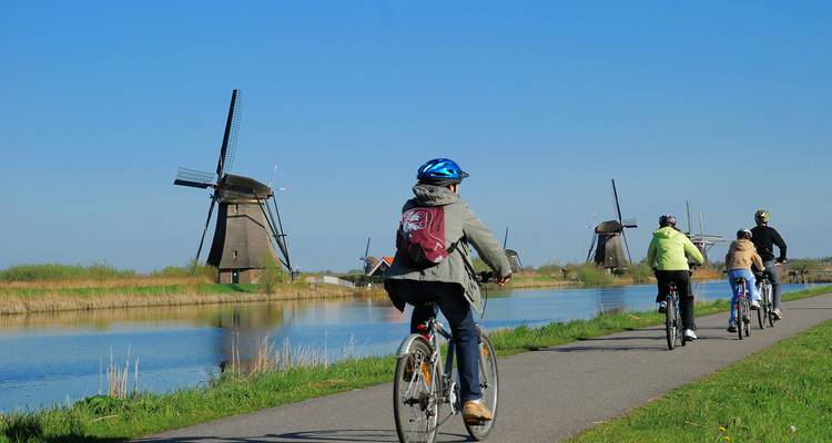 Radfahrer treten in die Pedale entlang des Kanals vorbei an ikonischen Windmühlen unter klarem blauen Himmel