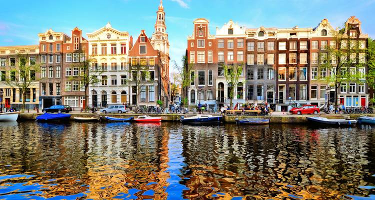 Reihe klassischer Amsterdamer Häuser, die sich bei goldener Stunde im Kanalwasser spiegeln