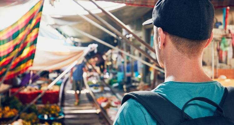 Vue arrière d'un voyageur avec un sac à dos observant les étals de produits animés le long des voies du marché ferroviaire.