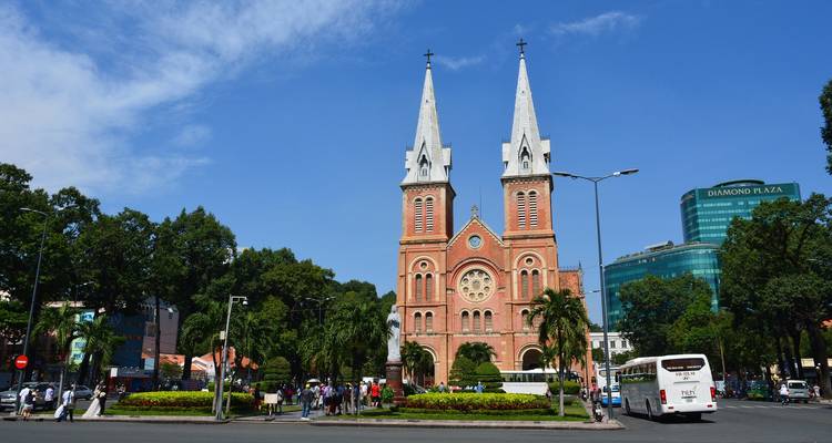 Vue de face de la Cathédrale Notre-Dame de Saigon sous un ciel bleu dégagé avec des piétons et du trafic