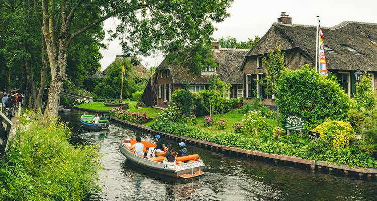 Kleines Motorboot mit Touristen, das durch einen engen Kanal fährt, der von Backsteinhäusern und Grünflächen in Giethoorn gesäumt ist.