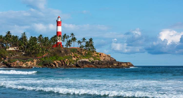 Faro rojo y blanco en un promontorio rocoso rodeado de palmeras que se eleva sobre las olas del océano azul.