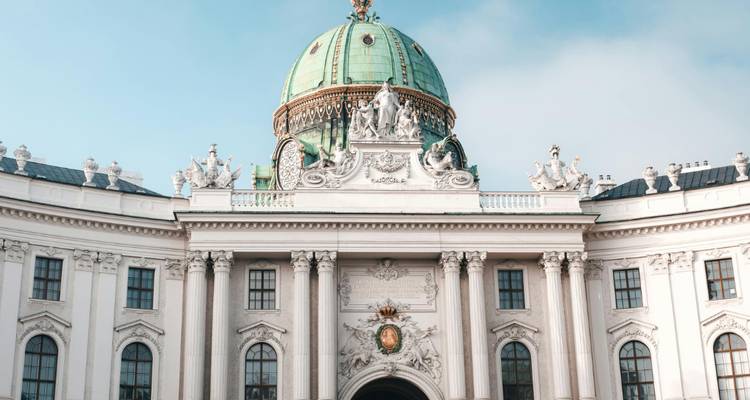 Facade baroque élégante du Hofburg de Vienne avec dôme en cuivre vert et statues sculptées sous un ciel bleu dégagé.