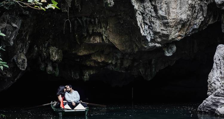 Couple dans une petite barque partageant un moment de tranquillité à l'entrée d'une grotte calcaire obscure à Ninh Binh.
