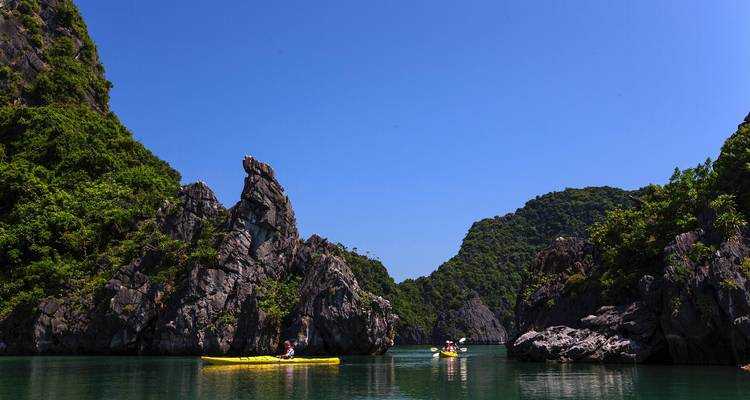 Les kayakistes pagaient entre les îles de calcaire karstique spectaculaires par une belle journée bleue dans la baie d'Halong.