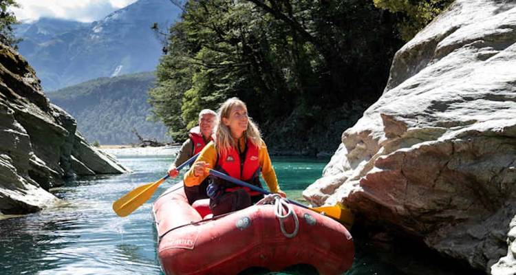 Deux pagayeurs manoeuvrant un radeau pneumatique rouge dans les eaux cristallines d'un canyon avec des montagnes boisées en arrière-plan