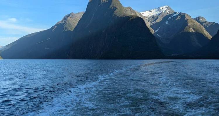 Sillage derrière un bateau traversant le Milford Sound avec ses falaises imposantes et ses pics enneigés