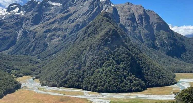 Pic pyramidal acéré couvert de forêts s'élevant à côté d'une vallée glaciaire sous un ciel dégagé