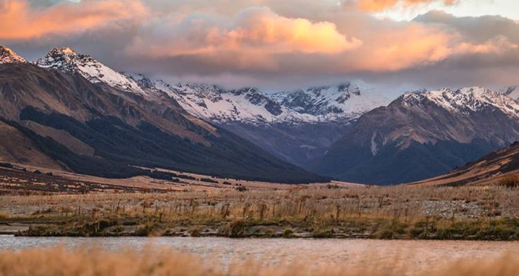 La lumière dorée du coucher de soleil baigne les chaînes de montagnes enneigées et une large vallée de prairies de touffes.