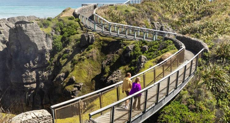 Une passerelle surélevée serpente le long de falaises côtières spectaculaires et de formations rocheuses aux côtés de la mer bleue.