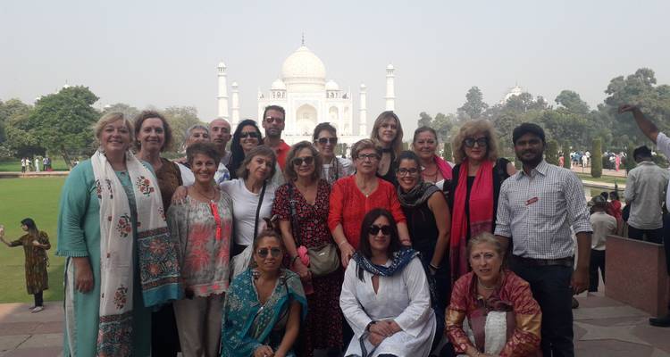 Eine große Reisegruppe posiert vor dem ikonischen weißen Marmor-Taj Mahal an einem dunstig-trüben Tag.