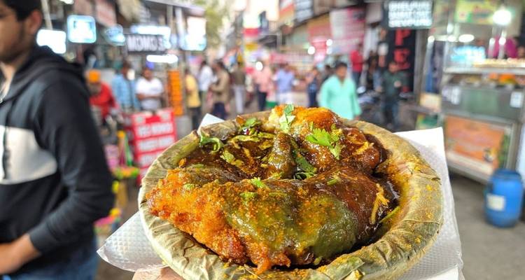 Primer plano de un plato picante de comida callejera servido en un cuenco de hojas con una concurrida calle del mercado borrosa de fondo.