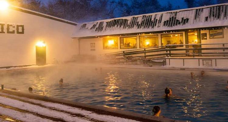 Les gens se détendent dans une piscine extérieure fumante lors d'une soirée hivernale enneigée.