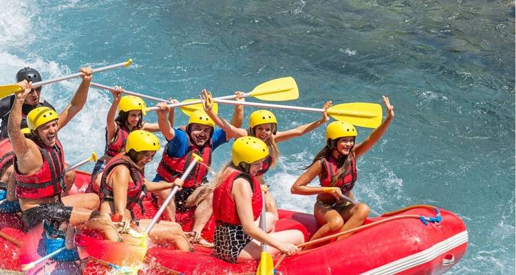 Remeros emocionados con cascos amarillos se lanzan por rápidos color turquesa en una balsa inflable