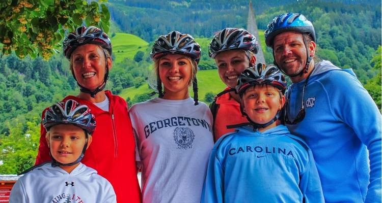 Familia sonriente de ciclistas usando cascos posa con hermosas colinas alpinas verdes de fondo