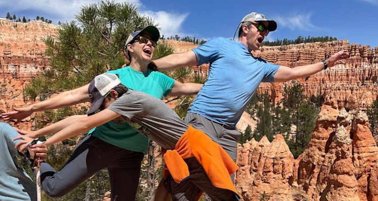 Trois voyageurs adoptent des poses ludiques sur les hoodoos orange et les pins de Bryce Canyon.