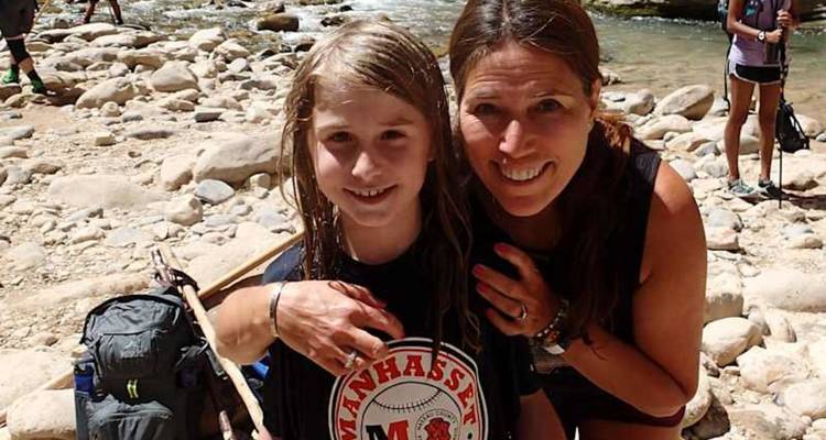 Une mère enlace son enfant aux cheveux mouillés à côté d'un ruisseau rocheux peu profond dans un canyon.