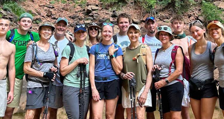 Un grand groupe de randonneurs portant des bâtons de trekking posent ensemble dans une rivière de canyon peu profond.