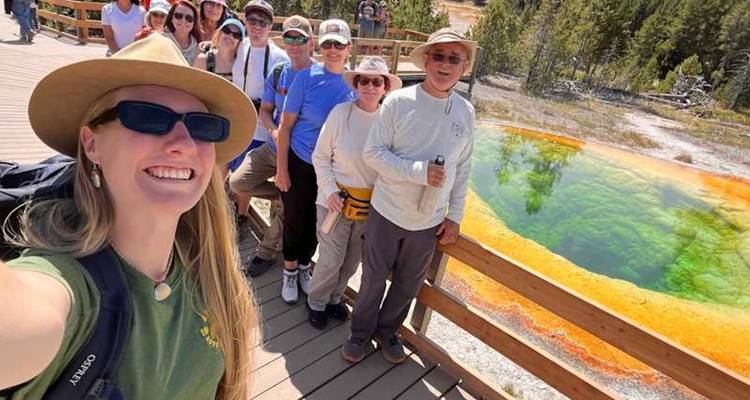 Un grupo de turismo sonriente se toma una selfie junto a una piscina de aguas termales de colores vivos.