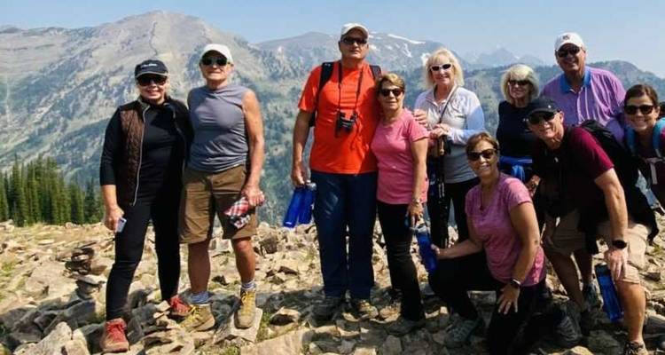 Groupe de randonneurs souriants posant sur un sommet alpin rocheux avec des chaînes de montagnes lointaines et brumeuses
