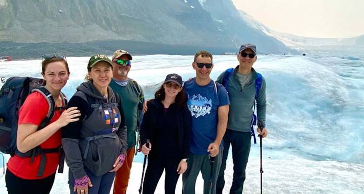 Un grupo de senderismo posa en un glaciar azul con bastones de trekking, con altas montañas asomándose detrás