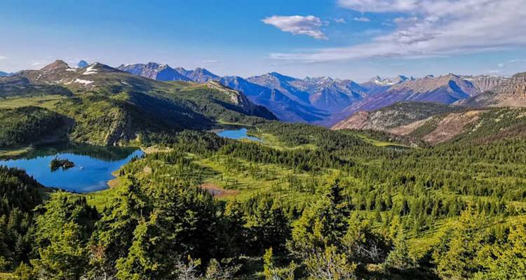 Panorámica expansiva de montaña con varios lagos azules rodeados de verdes prados alpinos ondulantes