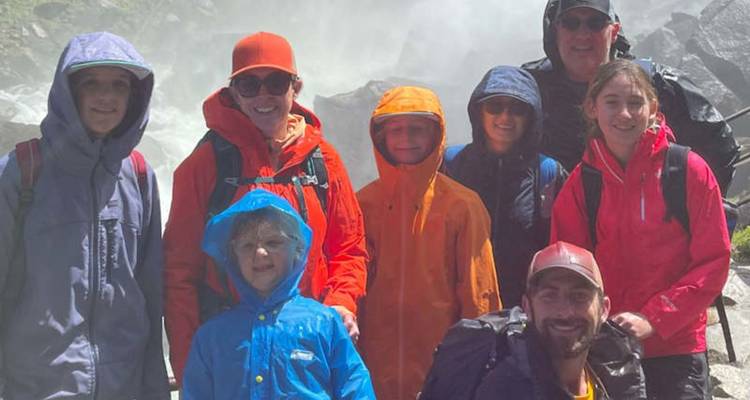 Une famille vêtue de vestes imperméables sourit devant une cascade brumeuse et un décor rocheux.