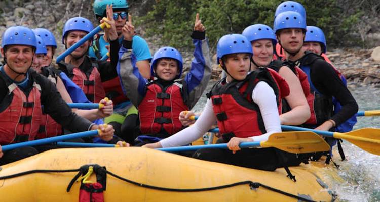 Los rafters de aguas blancas animan en una balsa amarilla en un río de montaña usando cascos azules.