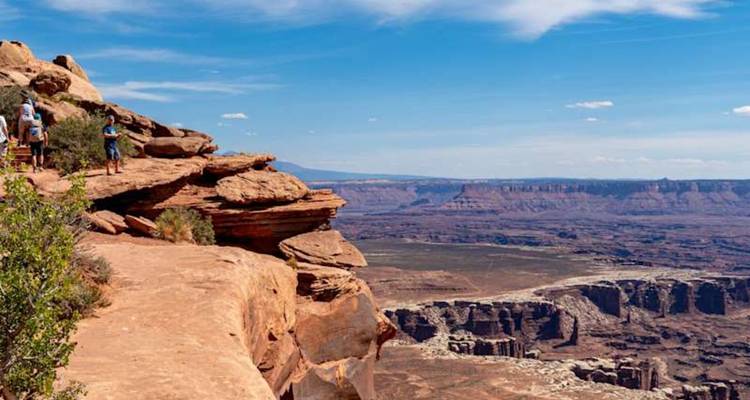 Les randonneurs font une pause sur le bord d'une falaise de grès surplombant une vaste vue de canyon désertique sous un ciel dégagé