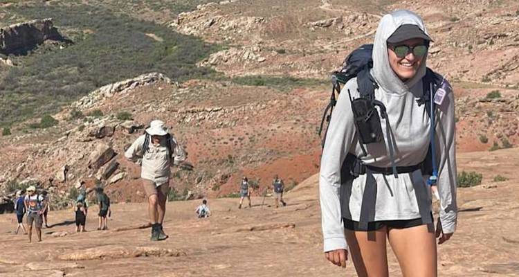 Une file de randonneurs gravit une pente désertique rocheuse avec des sacs à dos sous un fort ensoleillement et un terrain aride
