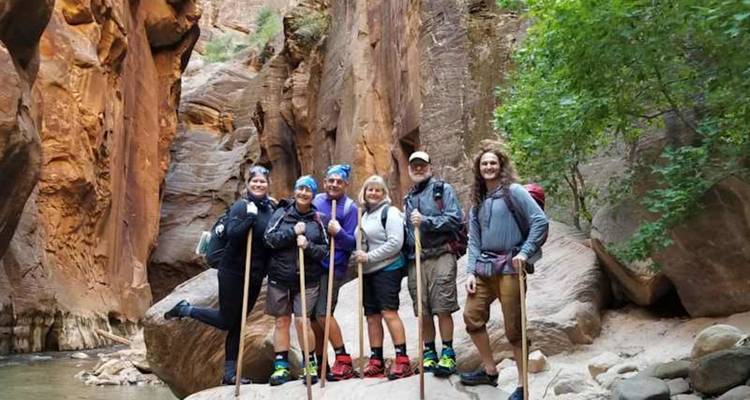 Un groupe de randonneurs traverse à gué les Gorges étroites entre des parois de canyon orange vertigineux.