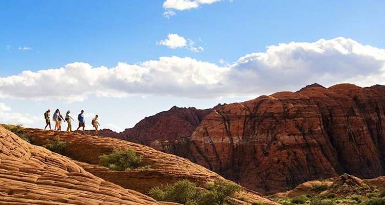 Les randonneurs marchent le long d'une crête de grès courbe sous un ciel désertique lumineux dans Snow Canyon.