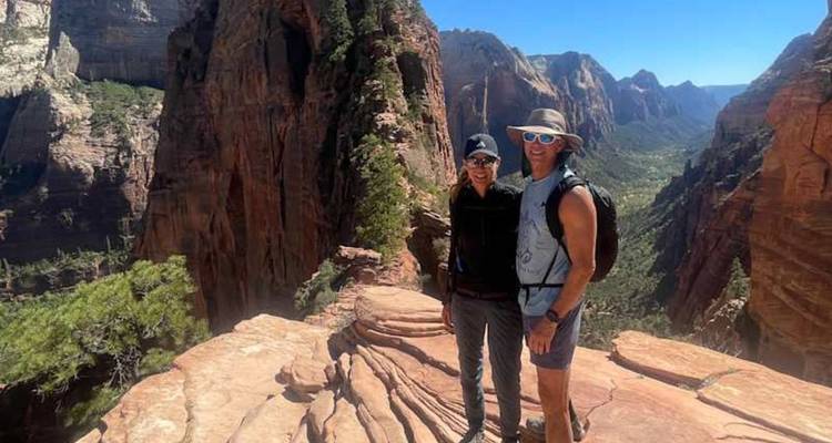 Un couple se tient sur un promontoire de grès élevé avec de vastes vistas de canyon à Zion.