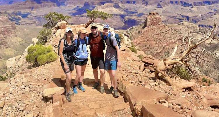 Trois randonneurs se tiennent sur un sentier rocailleux avec vue sur l'immense étendue du Grand Canyon.