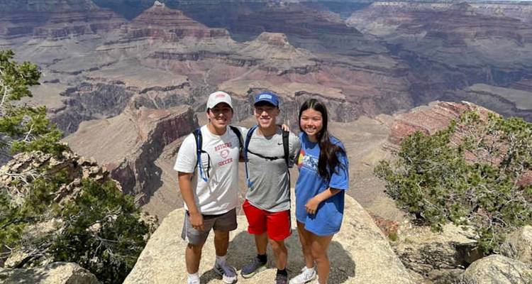 Trois voyageurs sourient au bord d'une falaise avec les vues en couches du Grand Canyon derrière eux.