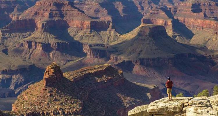 Un visiteur solitaire se tient sur un affleurement calcaire dominant les buttes en couches du Grand Canyon.