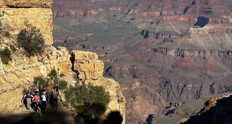 Un groupe de trekkeurs salue depuis une étroite corniche surplombant largement le fond du Grand Canyon.