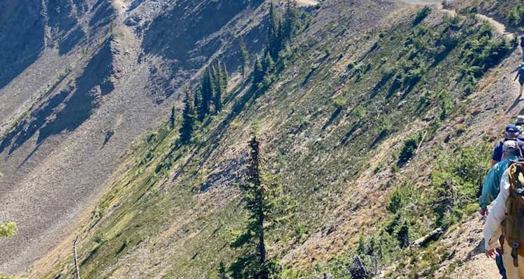 Les randonneurs parcourent un sentier montagneux étroit à grande altitude au-dessus d'une pente abrupte.