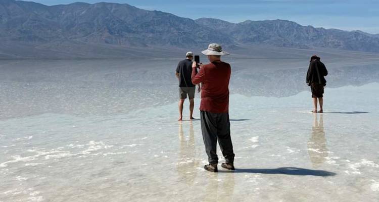 Les visiteurs se tiennent pieds nus sur un désert de sel réfléchissant en capturant des photos avec des montagnes grises lointaines en arrière-plan