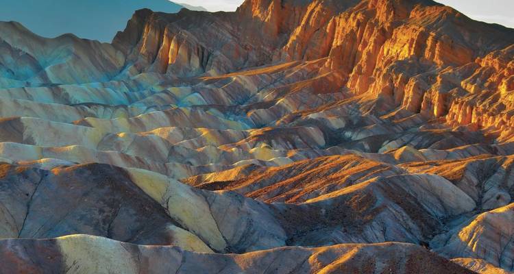 Les badlands colorés et stratifiés brillent sous une lumière rasante révélant les crêtes et les vallées du terrain de la Vallée de la Mort
