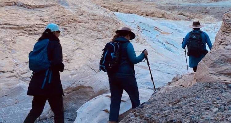 Trois randonneurs munis de bâtons de trekking se déplacent à travers un canyon rocheux étroit aux parois en couches