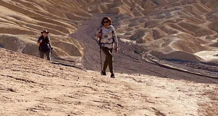 Les randonneurs montent péniblement une crête de terre beige desséchée par le soleil, avec des collines érodées s'étendant en arrière-plan