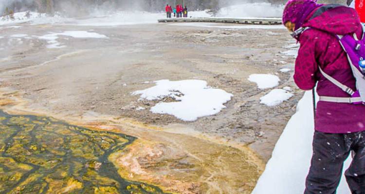 Un visiteur photographie une piscine thermale fumante bordée de neige.