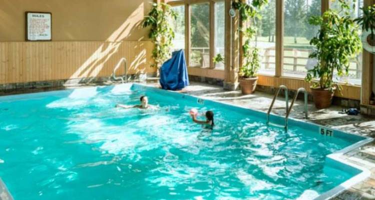 Piscine couverte d'hôtel éclairée par la lumière du soleil traversant les fenêtres avec deux personnes nageant