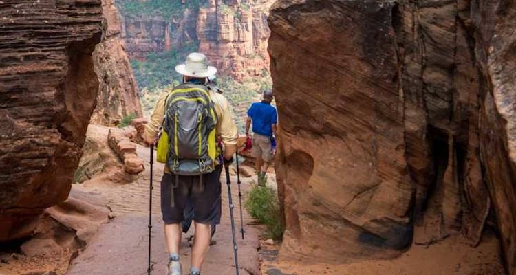 Un trekkeur avec des bâtons marche à travers un étroit passage en grès avec des compagnons devant lui.