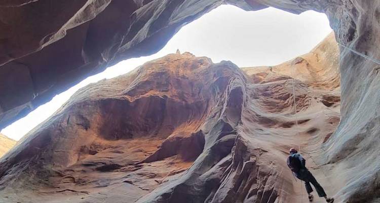 Un aventurier descend en rappel les hauts murs d'un canyon étroit baigné de soleil.