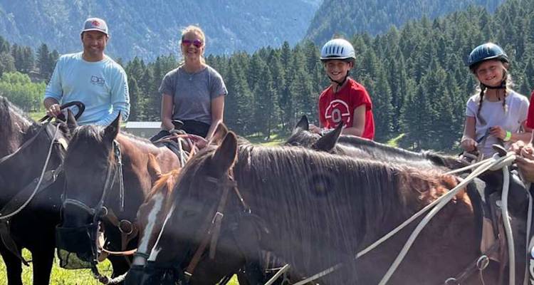 Des enfants et un adulte sont assis à cheval, prêts pour une randonnée équestre avec des montagnes boisées en arrière-plan.
