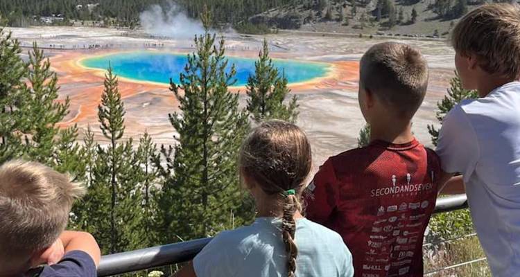 Des enfants regardent par-dessus une balustrade le vibrante Grand Prismatic Spring à Yellowstone.